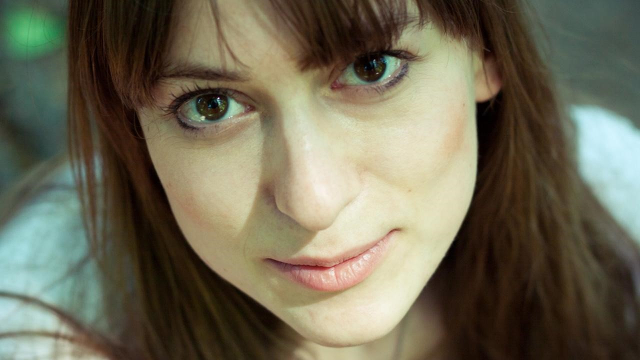 Nahaufnahme einer Person mit braunen Haaren und lebhaften Augen, die direkt in die Kamera blickt.