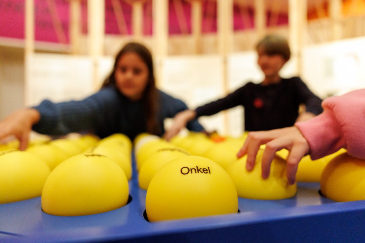 Kinder spielen mit gelben Bällen auf einem blauen Tisch, auf dem verschiedene Wörter stehen.