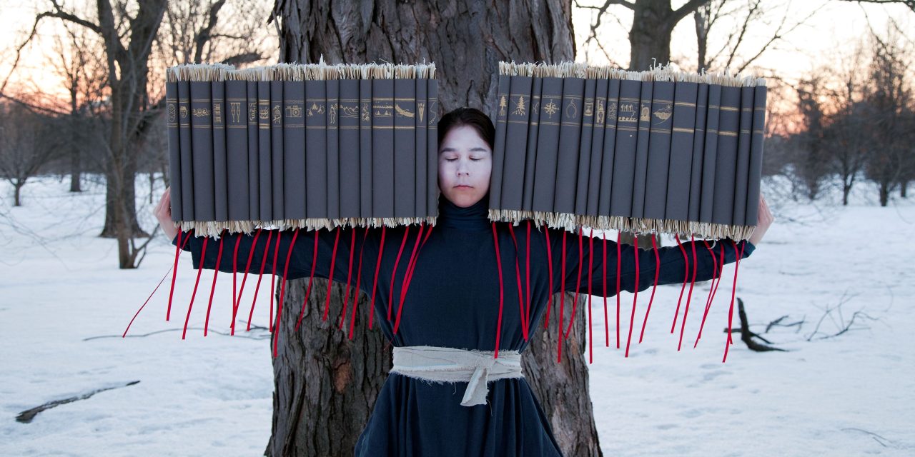 A person stands in front of a tree, holding books with red ribbons, surrounded by snow and blooming light.