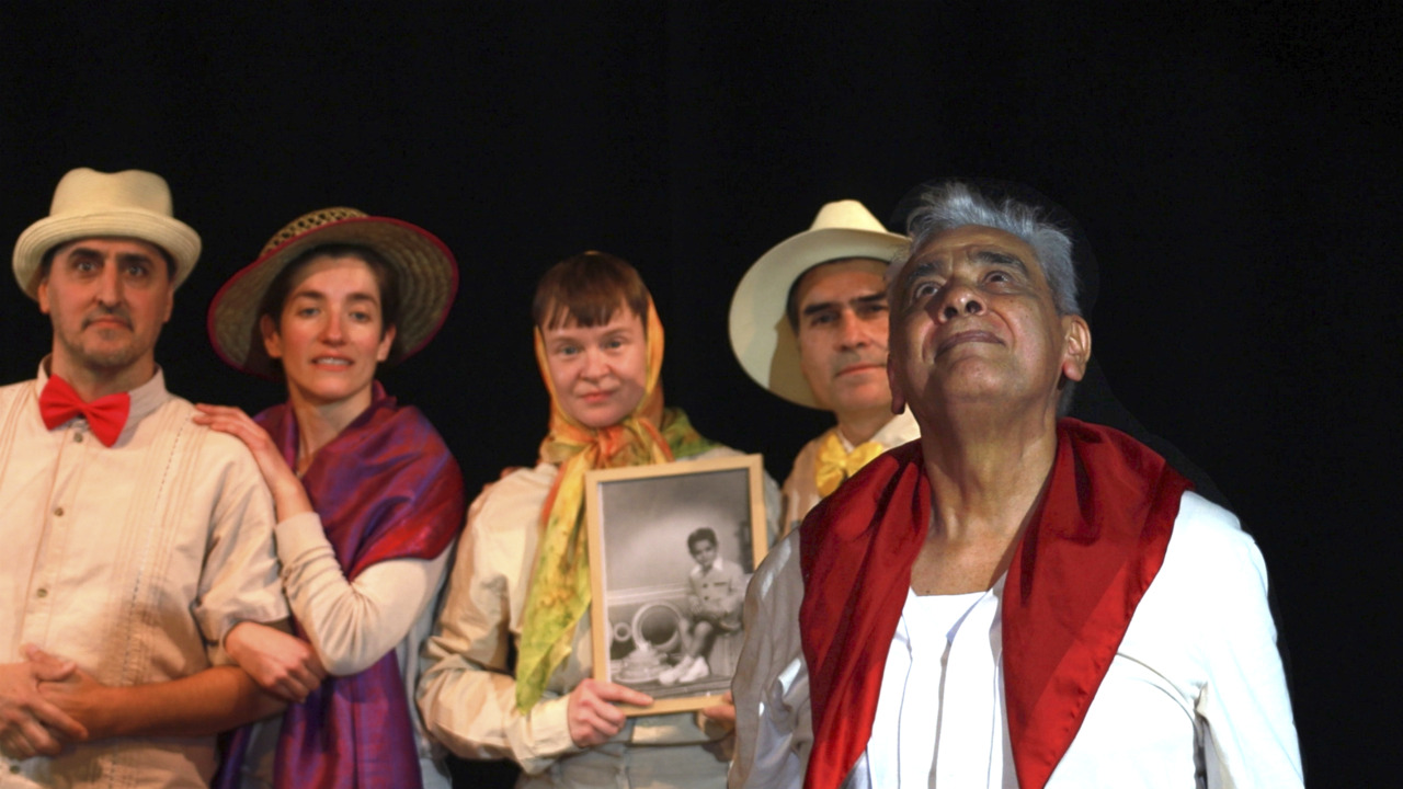 Fünf Personen in historischen Kostümen posieren auf einer Bühne, ein Porträt in der Mitte, während einer nach oben schaut.