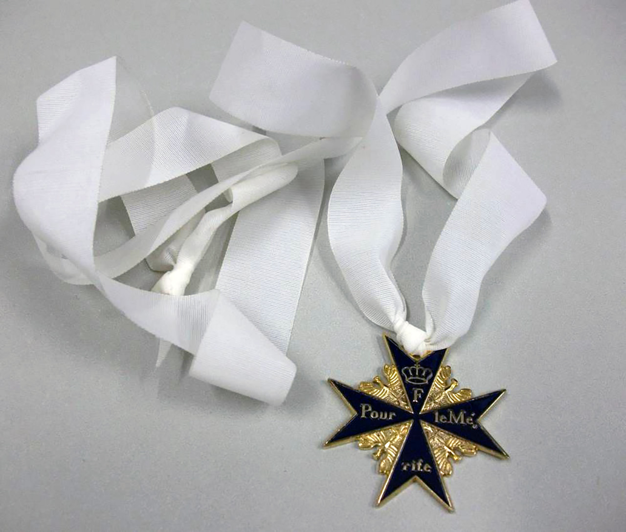 Goldmedaille mit blauen Akzenten und weißen Bändern, beschriftet mit „Pour le Mérite“.