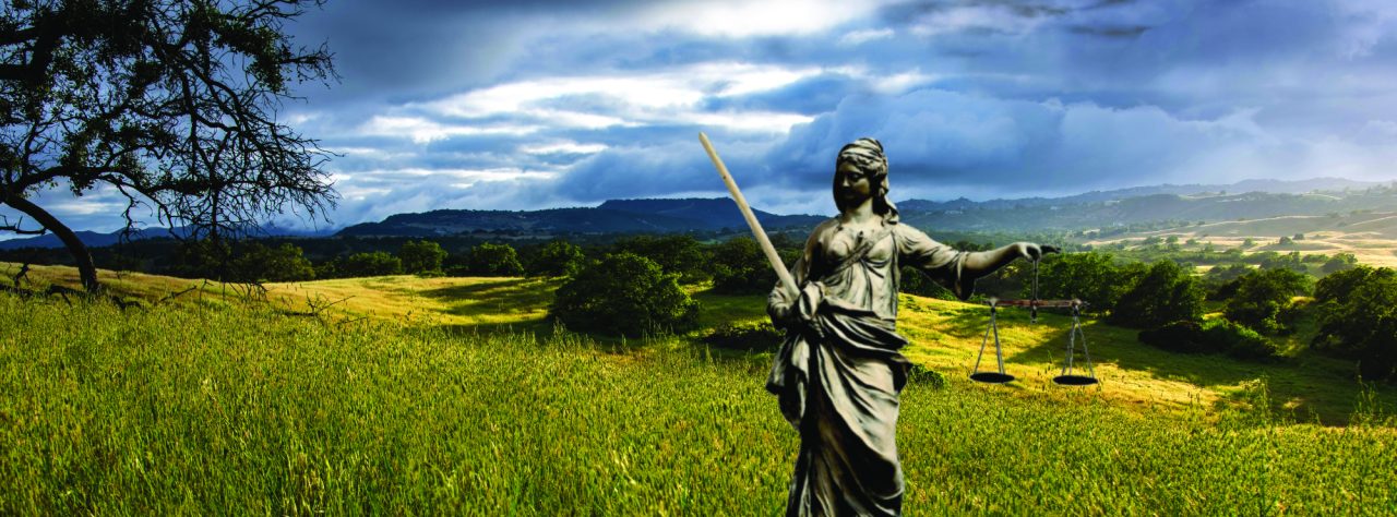 A statue of Justice stands in a vast landscape under a cloudy sky.