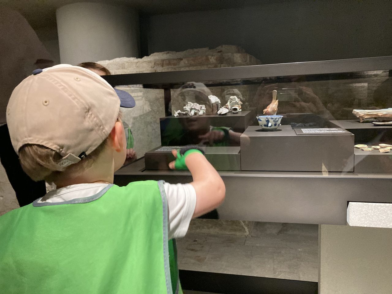 A child in a green vest looks at exhibits behind glass in a museum.