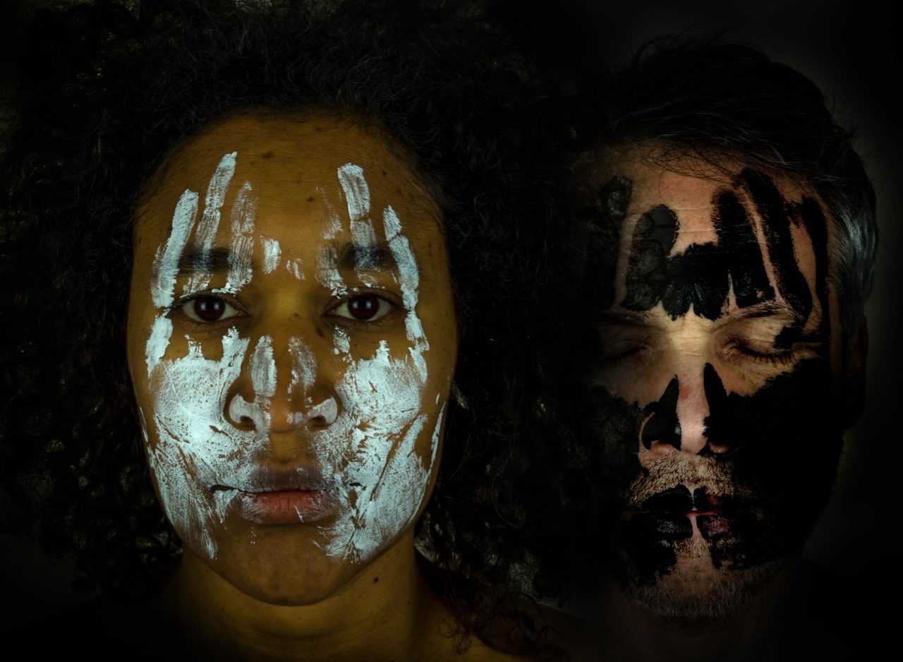 A contrasting portrait of two people, one with white face paint and the other with black face paint.