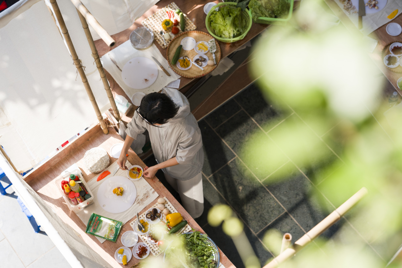 Person in grauem Outfit bereitet mit frischen Zutaten ein Gericht an einem vorbereiteten Arbeitsplatz im Freien vor.