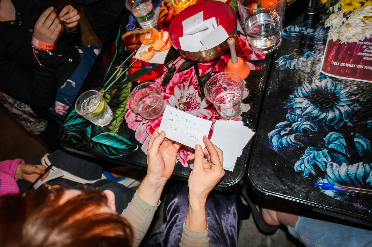 Hands hold a message surrounded by drinks and notes on a colorfully decorated table.