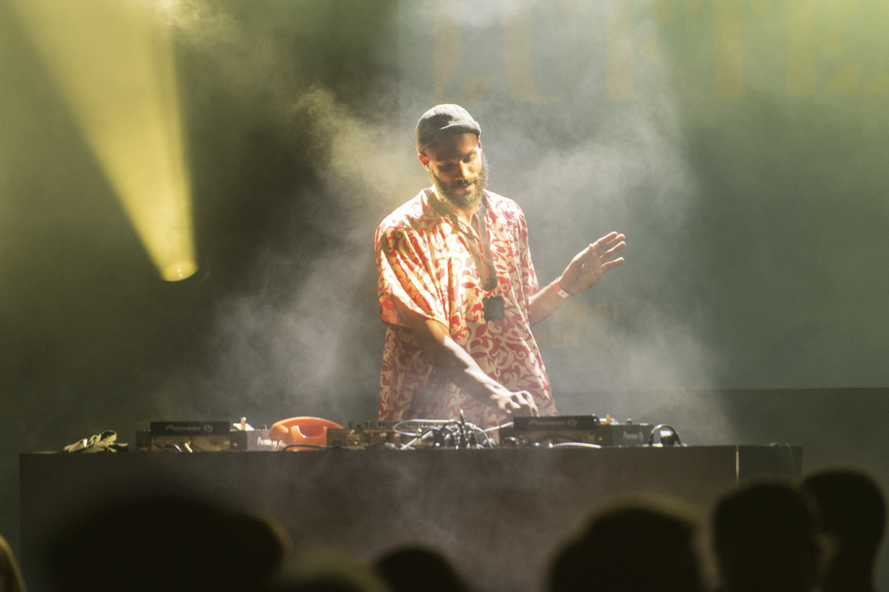 DJ at a live performance, surrounded by fog and colorful lights, while mixing music.