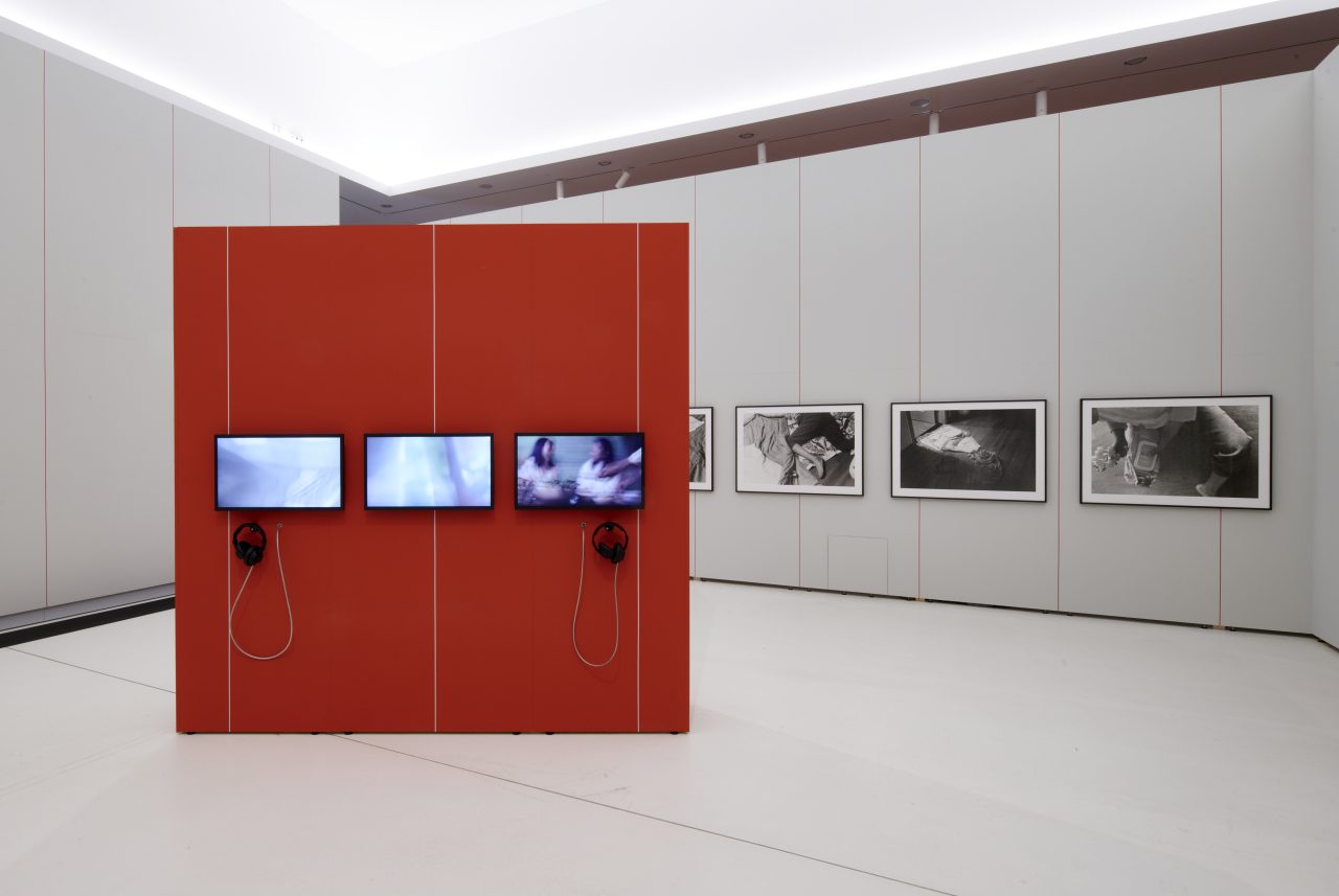 Interior of an art gallery with red walls, screens, and photographs on the walls. Minimalist design.