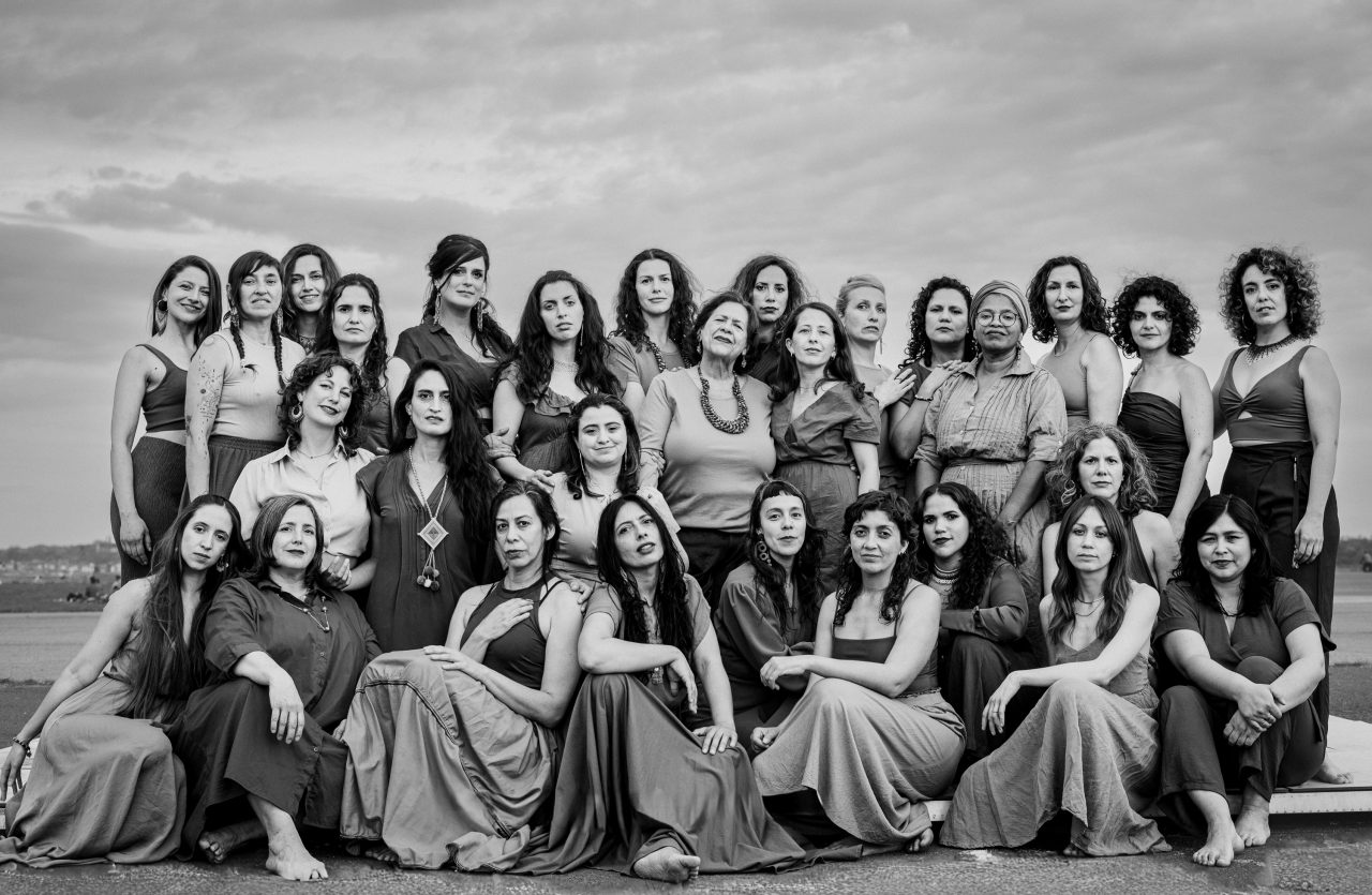 Gruppennahaufnahme von elegant gekleideten Frauen in Schwarz-Weiß vor einem bewölkten Himmel.