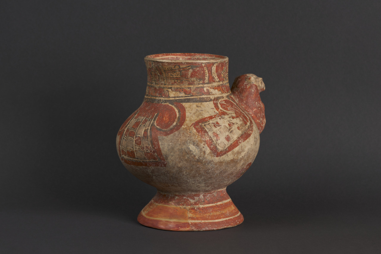 Terracotta-Krug mit rot-weißer Bemalung und Tierkopf-Applikation auf schwarzem Hintergrund.