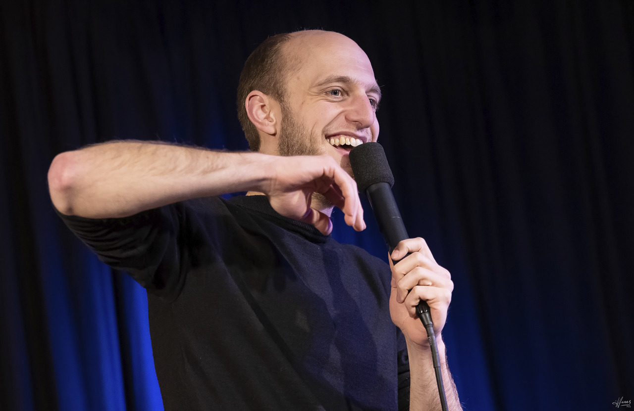 Poetry-Slam-Meister Alex Burkhardauf der Bühne mit Mikrofon interagiert entspannt mit dem Publikum.