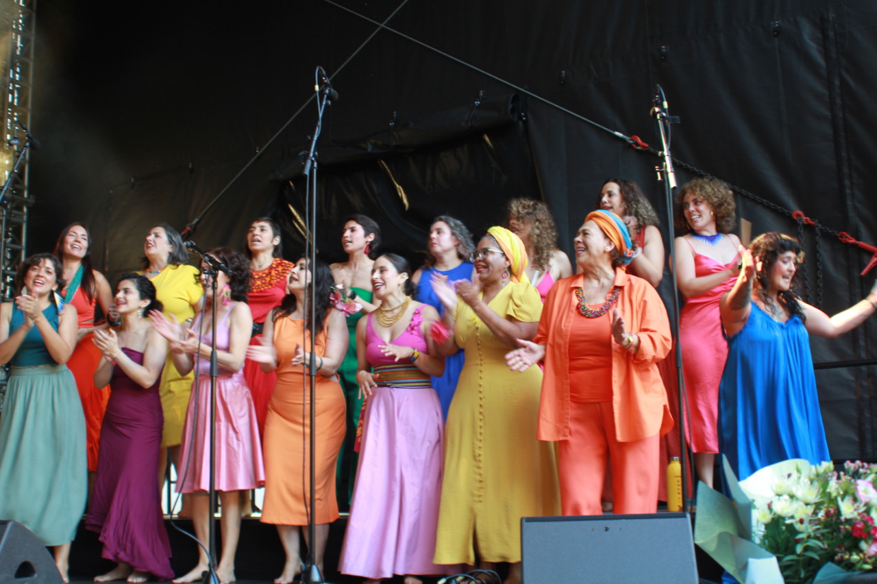 A vibrant women's choir community sings and dances on stage, full of joy and energy during a live performance.