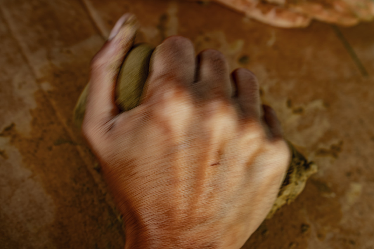 A hand kneads a clay-like material on a wooden surface.